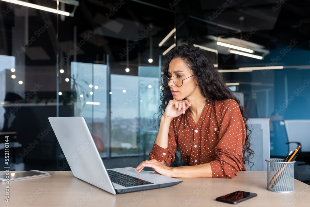 Woman looking at laptop with hand in a fist under her hand trying to make a decision on security companies.